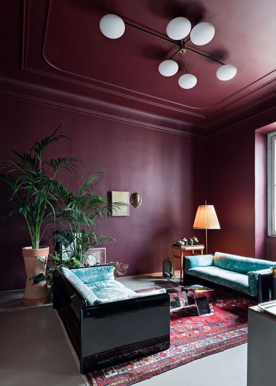 a purple living room with a purple ceiling, turquoise velvet sofas, a coffee table, a printed rug and potted plants