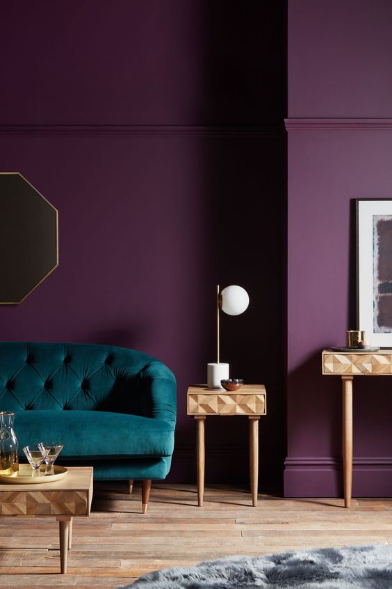 a purple living room with a teal sofa, inlay mini side tables, a grey rug and a mirror in a hex frame in gold