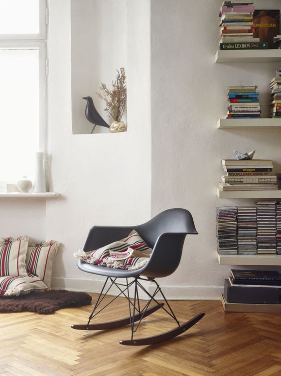 a reading nook by the window, with bookshelves, a grey Eames rocker and some pillows right on the floor