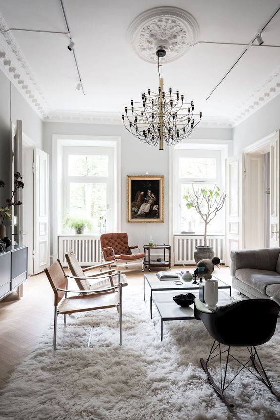 a refined Parisian living room with a grey sofa, a couple of coffee tables, brown leather chairs and a black Eames rocker plus a bold chandelier