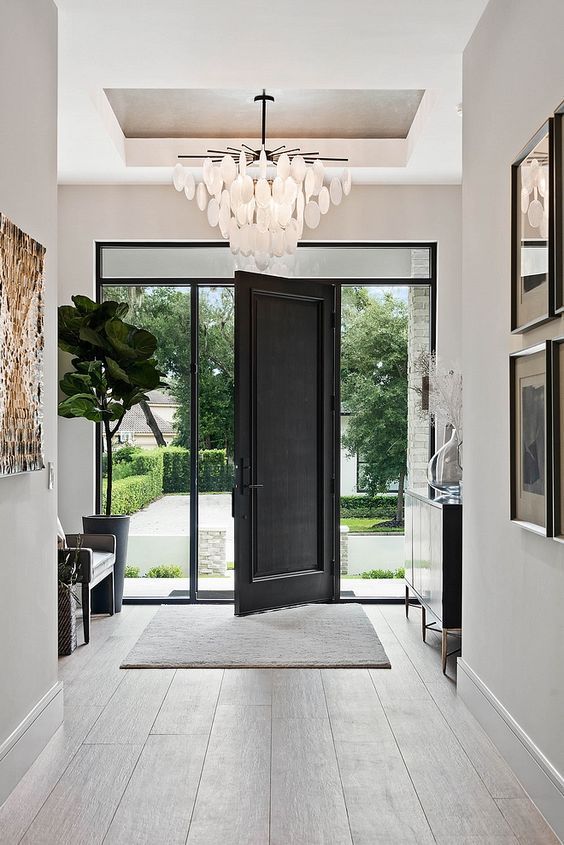 a refined black and white entryway with a black door and glass, a black bench and a console, a cool chandelier and a statement potted plant