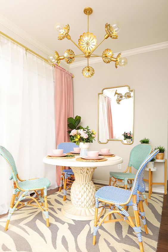 a refined dining room with neutral walls, a round table, pastel chairs, a gold chandelier and a printed rug plus pink curtains