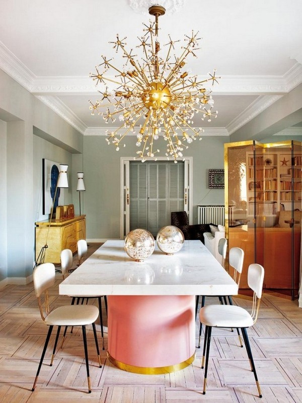 a refined dining room with pastel green walls, a large table with a pastel pink base, neutral chairs and a gold chandelier