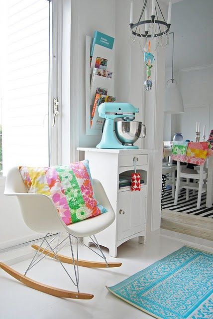 a retro space with white furniture including a white Eames rocking chair and some turquoise and colorful touches