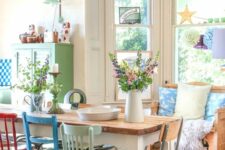 a shabby chic dining space with a loveseat at the bay window, a stained table and mismatching colorful and pastel chairs, an aqua pendant lamp