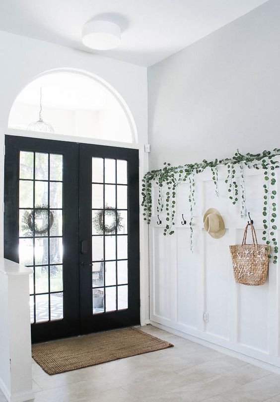 a simple black and white entryway with black French doors, white paneling, greenery and a rack integrated into paneling