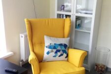 a small nook with a glass storage unit, a yellow Strandmon chair, a black coffee table and a printed pillow is a stylish space