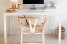 a small working space with a sleek white desk, a light-stained wishbone chair, a table lamp and a small basket for storage