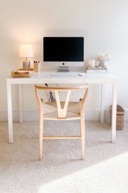 A small working space with a sleek white desk, a light stained wishbone chair, a table lamp and a small basket for storage