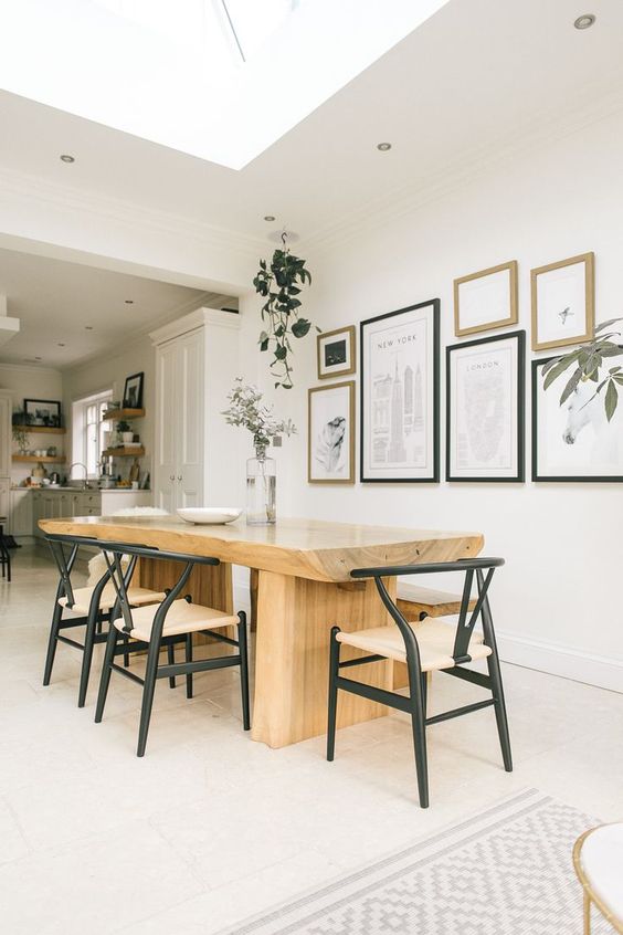 a sophisticated modern dining space with a large stained table, black wishbone chairs, a gallery wall and potted greenery