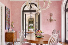 a sophisticated pastel pink dining room with a stained credenza, an oval table, pink chairs, a bold artwork and a printed rug