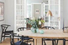 a stylish Scandinavian dining room with a light-stained oval table and black wishbone chairs, elegant copper pendant lamps