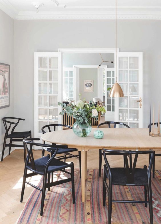 A stylish Scandinavian dining room with a light stained oval table and black wishbone chairs, elegant copper pendant lamps
