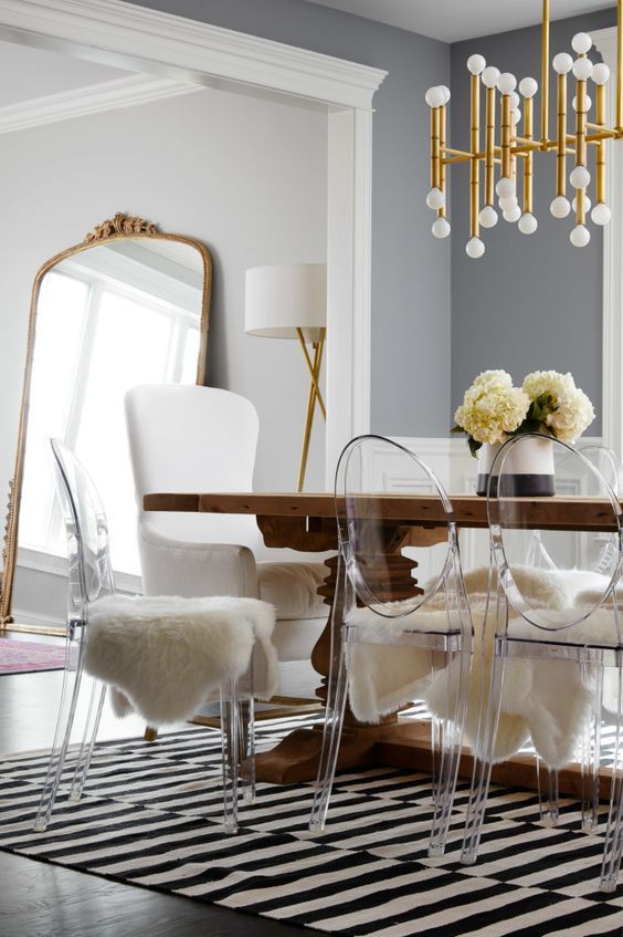 a stylish Scandinavian dining space with grey walls,a  heavey stained dining table, ghost chairs with faux fur and a gilded chandelier