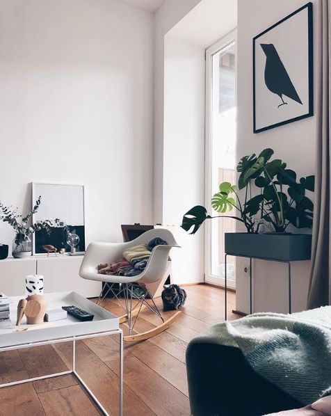 a stylish Scandinavian living room with a white Eames chair, a white coffee table, a plant stand and black and white artwork