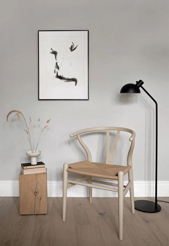 A stylish Scandinavian nook with a light stained wishbone chair, a stump side table, a black floor lamp and a wall art