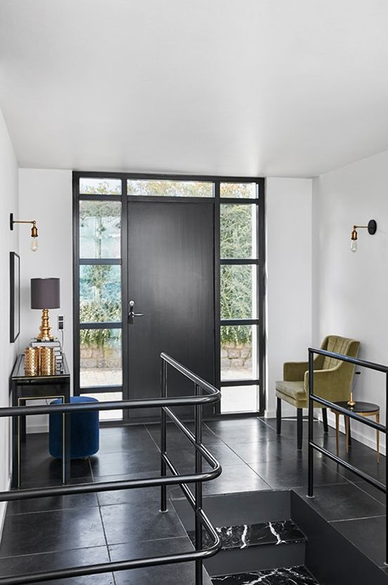 a stylish black and white entryway with a black door, a chic black console, a mustard chair and a blue pouf plus gilded touches