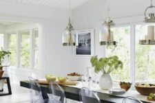 a stylish dining space with long black table, ghost chairs, pendant lamps with a gold rim and greenery