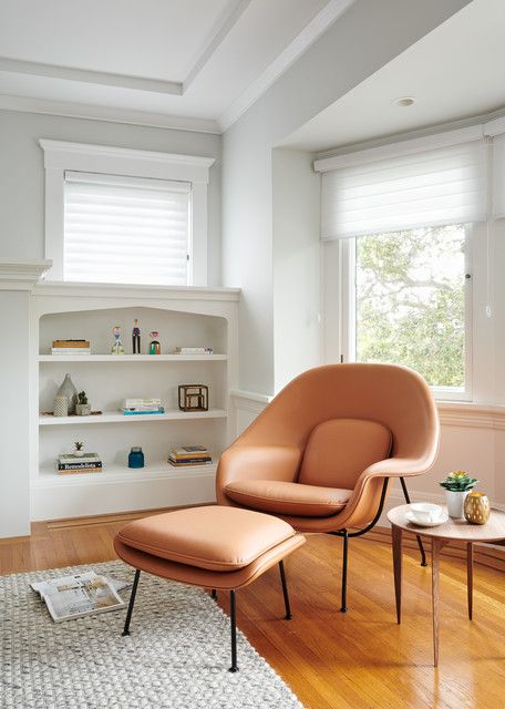A stylish nook with a built in shelving unit, an amber leather chair and ottoman, a side table and a rug us cozy and cool
