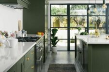 a stylish olive green kitchen with flat panel and shaker cabinets, white stone countertops and a backsplash, gold and brass knobs