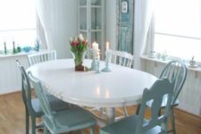 a sweet pastel blue and white dining space with a corner buffet, a white oval table, blue chairs, a blue chandelier and a shabby chic door