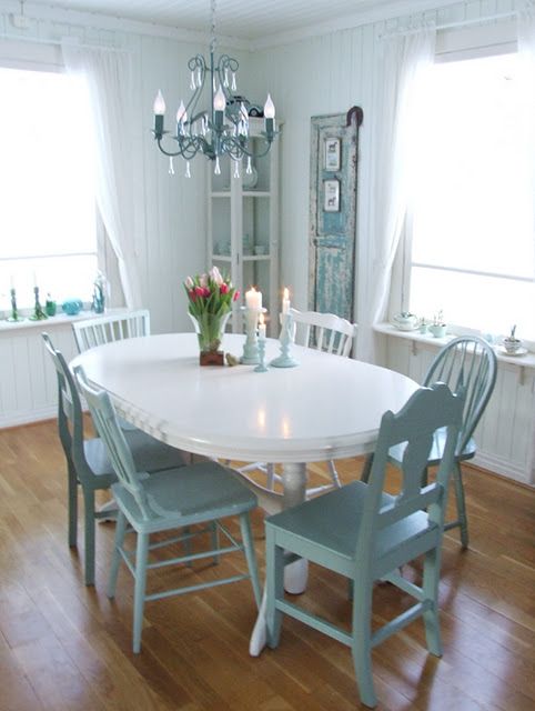a sweet pastel blue and white dining space with a corner buffet, a white oval table, blue chairs, a blue chandelier and a shabby chic door