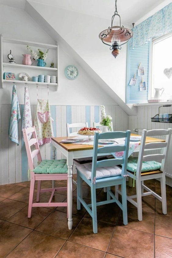 A vintage inspired pastel dining room with blue and white paneling, a vintage table and pastel chairs, blue shutters and a curtain plus pastel towels