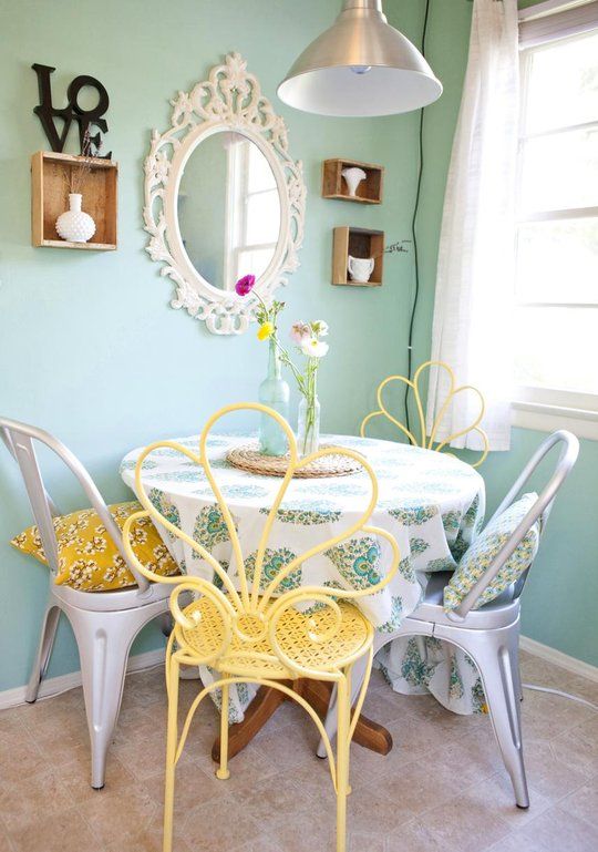 a vintage pastel dining nook with pastel green walls, a round table and mismatching chairs - metal and yellow ones, some shabby chic decor on the wall