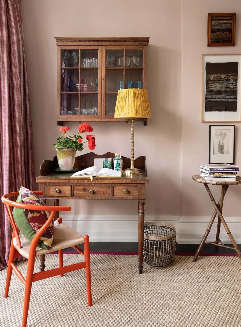 A vintage working space with a dark stained desk and a cabinet, an orange wishbone chair and a side table, some art