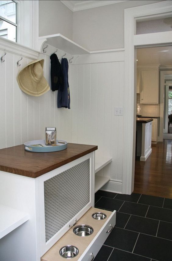 A white farmhouse mudroom with built in shelves, a console table that features a dog crate and a drawer with bowls