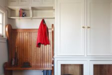 a white mudroom with a brick floor, creamy cabinets, a stained rack and a built-in dog crate in the lower part