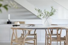 an airy Scandinavian dining space with a white dining table, light-stained wishbone chairs, a sleek storage unit and greenery