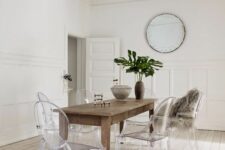 an airy dining room with a stained table, ghost chairs, a crystal chandelier and a round mirror plus statement leaves