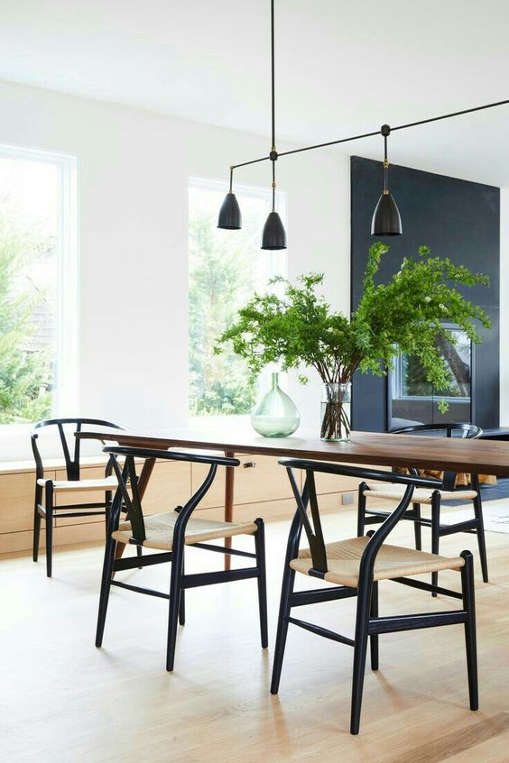 An airy dining space with a dark stained table and black wishbone chairs, a catchy black pendant lamp over the table