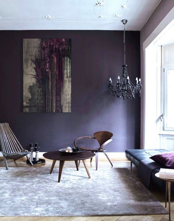 an eclectic living room with a black leather daybed, a couple of wooden chairs and a table, a black chandelier and a deep violet accent wall