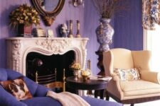 an elegant and chic living room with purple walls, a violet daybed, a neutral chair, a French fireplace, vintage sconces and a mirror