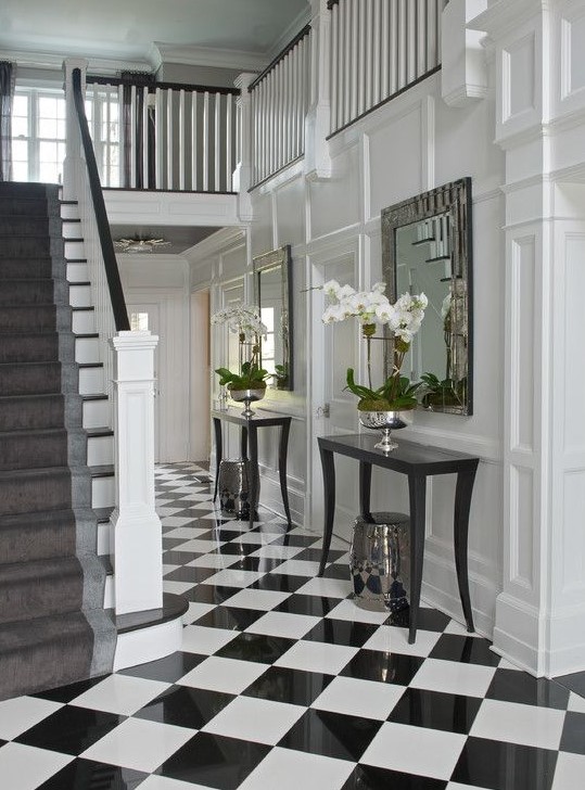an elegant black and white foyer with checked tiles, black console tables, mirrors in chic frames and potted orchids