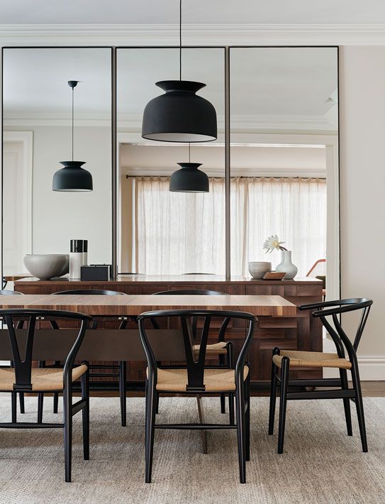 An elegant mid century modern dining space with a butcherblock dining table, black wishbone chairs, black pendant lamps and a large mirror