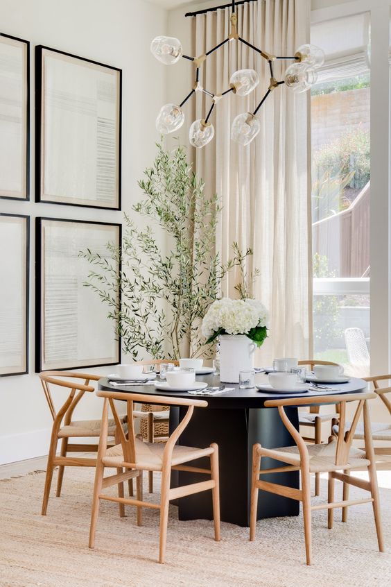 An elegant modern dining space with a black dining table and light stained chairs, a gallery wall and a catchy chandelier