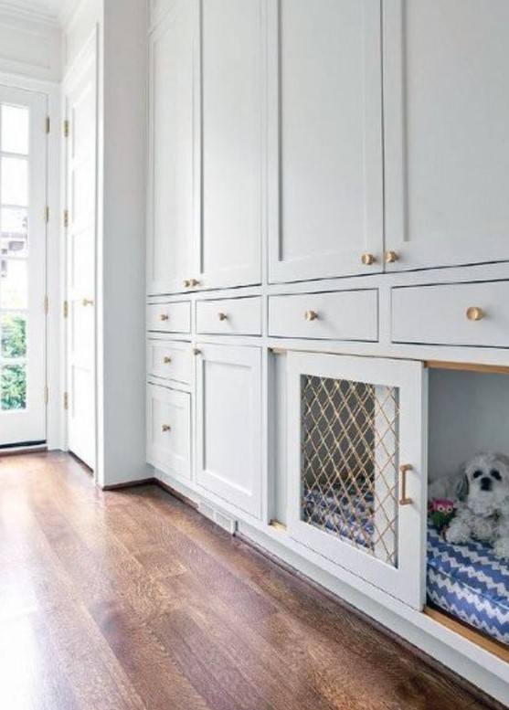 An elegant neutral mudroom done with off white shaker cabinets and a dog crate with a sliding door is a cool space
