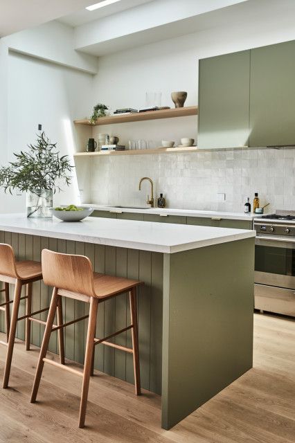 an elegant olive green farmhouse kitchen with white Zellige tiles on the backsplash, open shelves, wooden stools