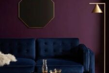 an exquisite living room with a deep purple accent wall, a navy sofa, a beautiful wooden coffee table and a gold floor lamp
