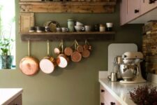 an olive green kitchen with pink shaker cabinets, black knobs, a reclaimed wood backsplash and open shelves