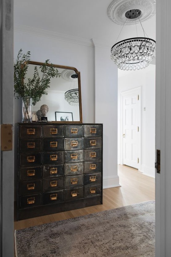 A dark stained shabby chic card cabinet, a mirror and greenery on it adds vintage chic to the entryway and makes it refined
