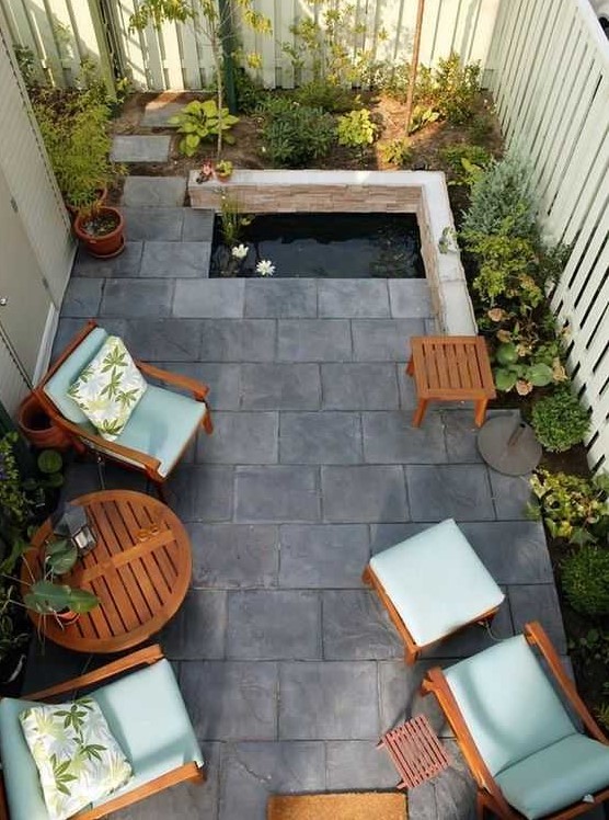 A small and zen like backyard with tiles on the ground, a tiny pond, some growing plants and cool garden furniture with blue upholstery