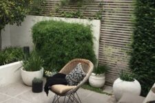 07 a contemporary walled backyard with a planked screen, with a tiled floor, potted grasses and greenery, a small dining set with pillows and a woven chair