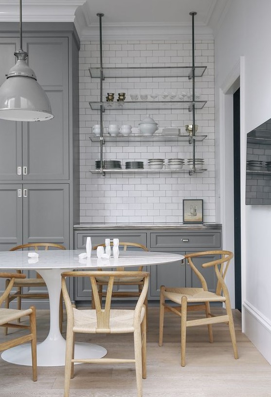 a grey farmhouse kitchen with a white subway tile backsplash, a suspended glass shelf, an oval table and stained chairs