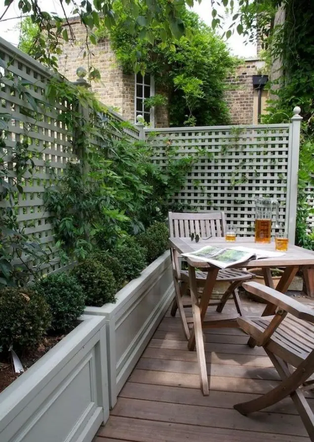 a small and cozy backyard with a deck, a simple wooden outdoor furniture set, potted greenery and climbing plants is very cozy