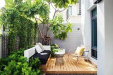 09 a small contemporary backyard with a wooden deck, a built-in daybed and a cool chair, some growing plants and a large living tree
