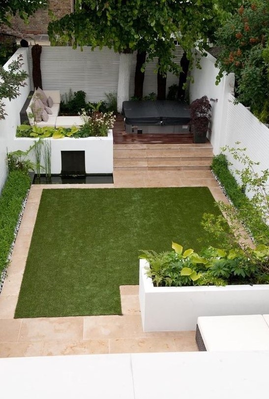 a minimalist townhouse garden with white flower beds with greenery, a tiny pond, a manicured lawn, a sectional sofa and a hot tub